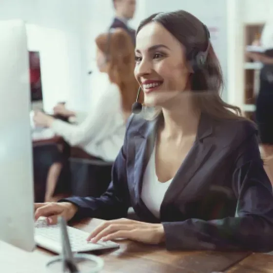 A woman wearing headphones is smiling while using a computer