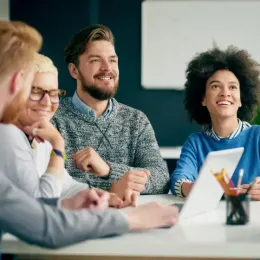 A group of people are sitting around a table with a laptop.