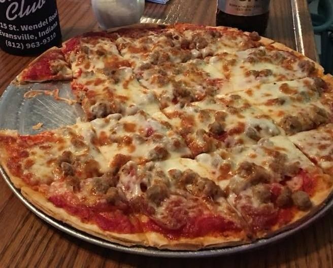 A pizza with a slice taken out of it is on a pan on a table.