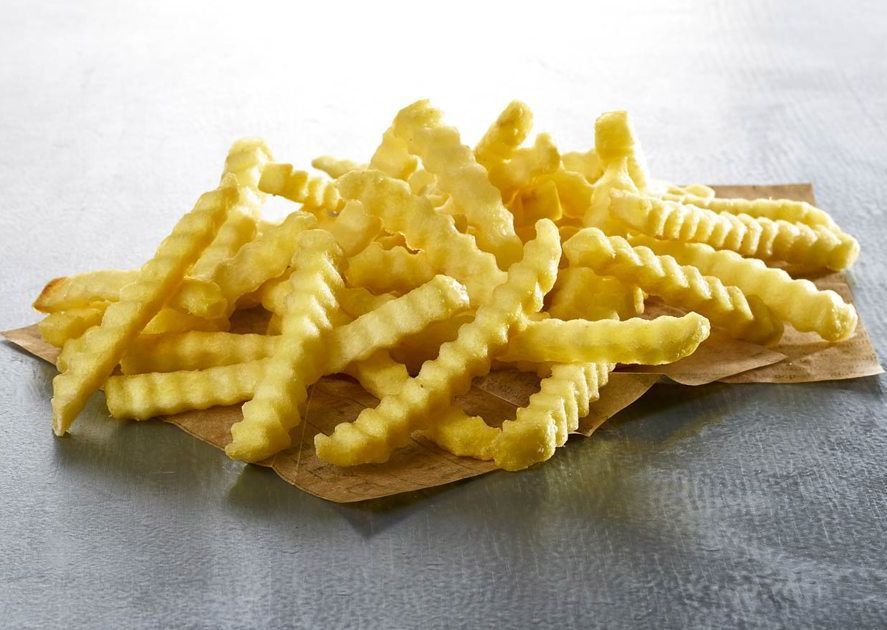 A pile of french fries on a piece of paper on a table.