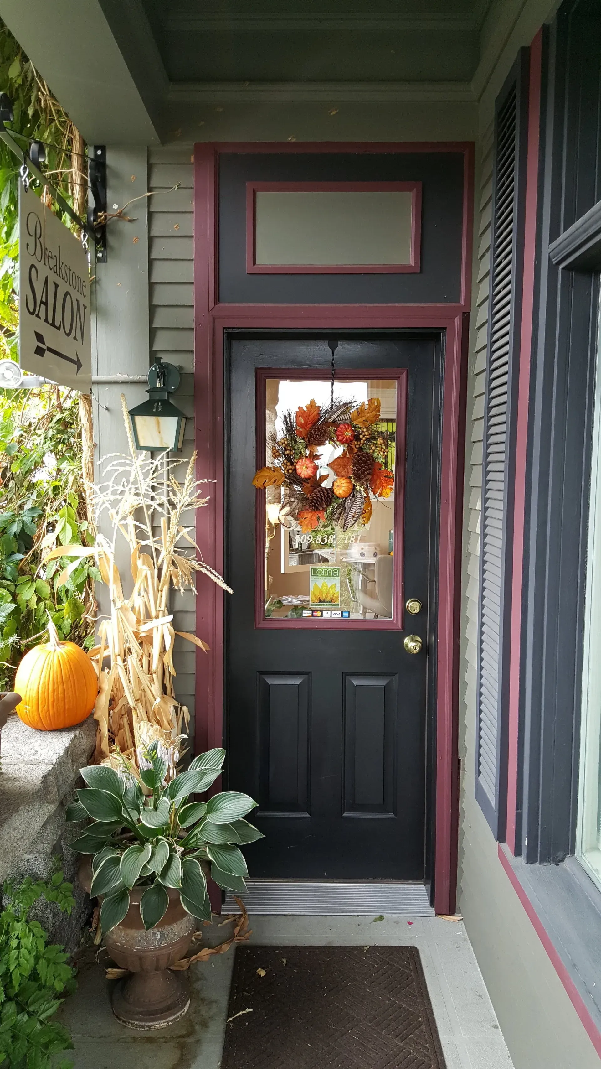 A black door with a wreath on it is on a porch.