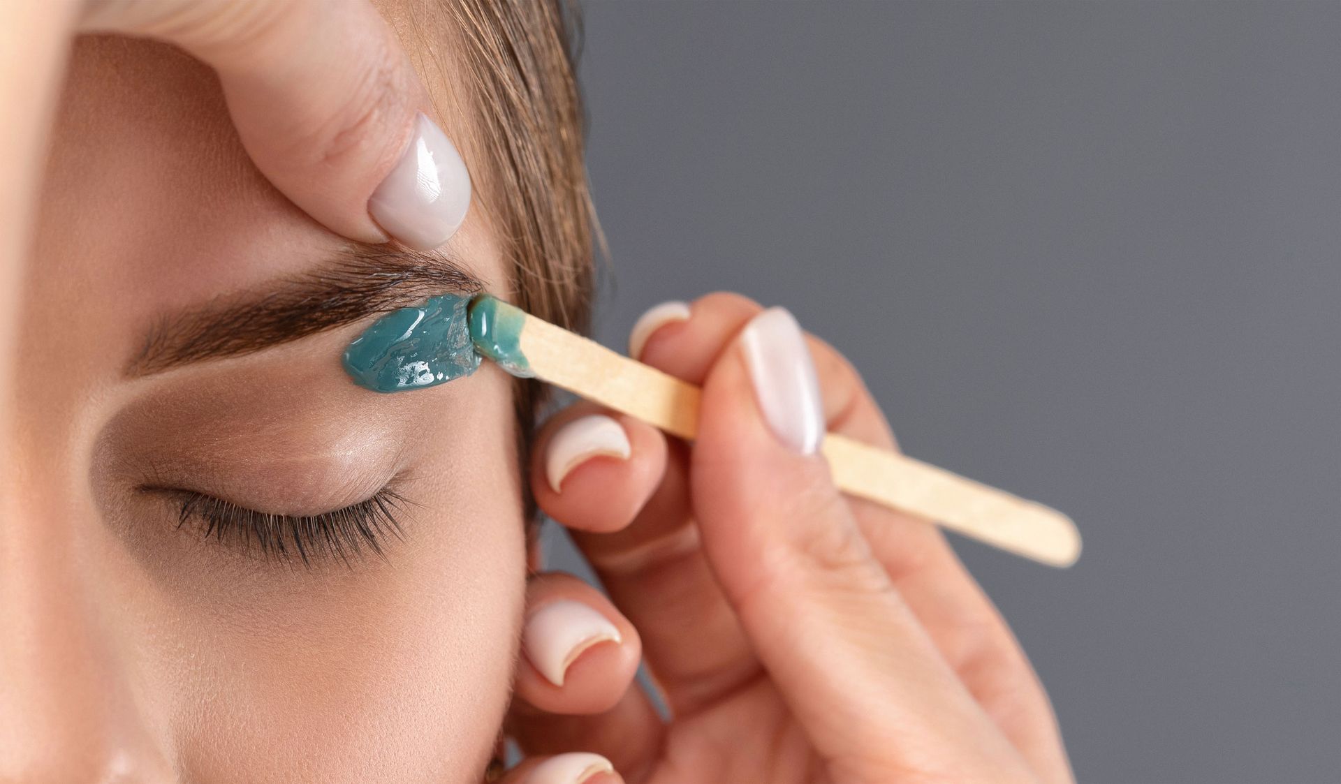 A woman is waxing her eyebrows with a stick.