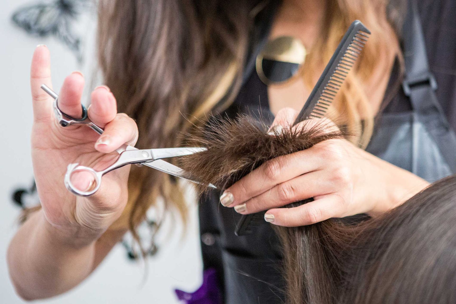 A woman is cutting a woman's hair with scissors and a comb.