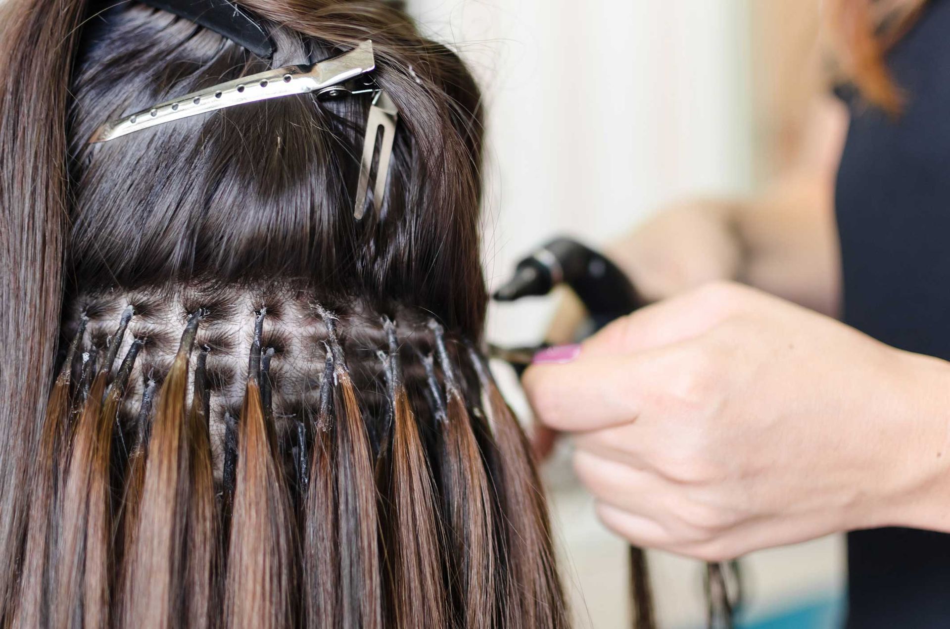 A woman is getting her hair extensions done by a hairdresser.