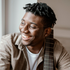 Smiling Black man with dreadlocks holding a guitar, near a window.