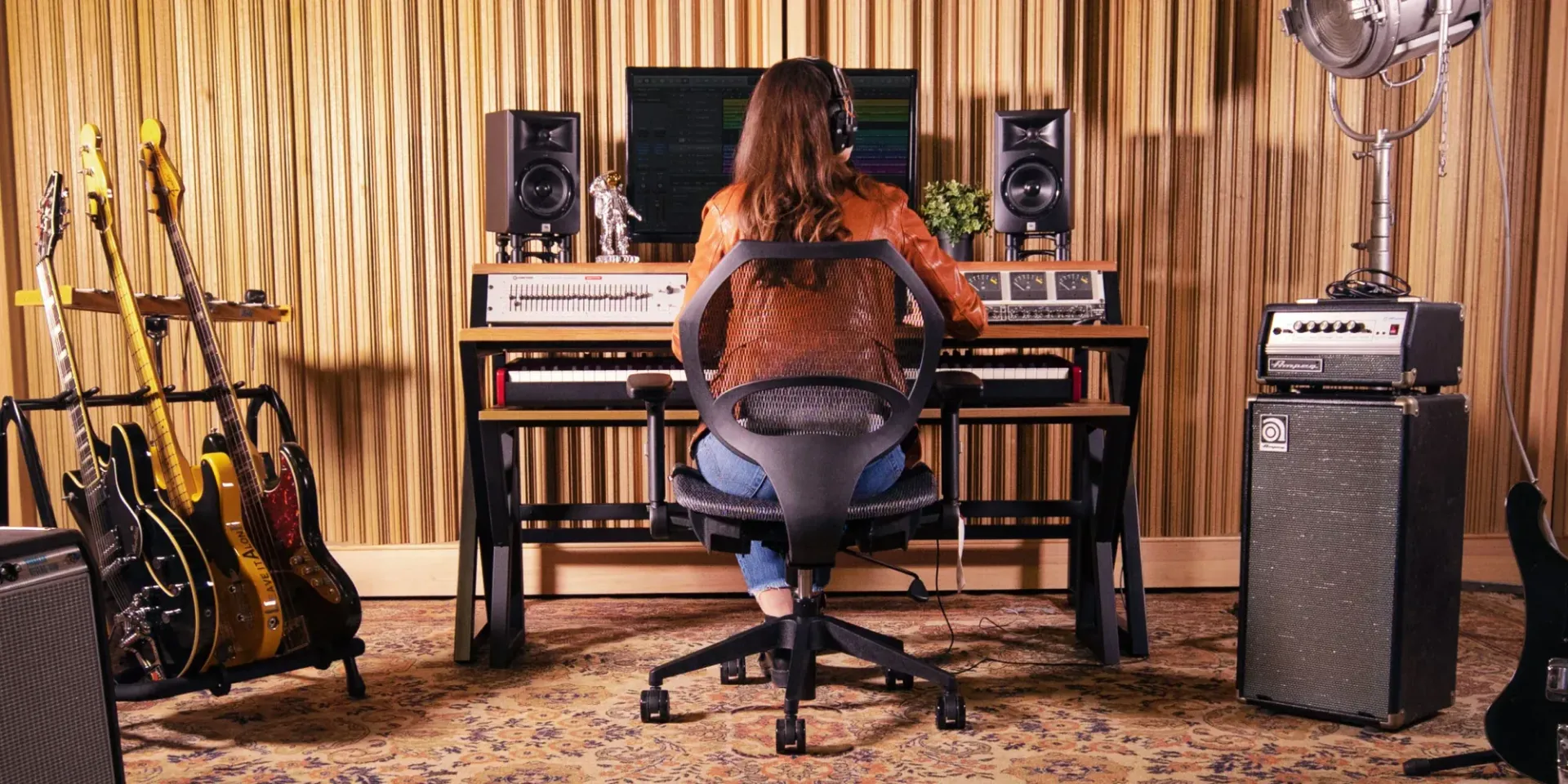 Woman wearing headphones at a mixing desk in a recording studio, guitars in the background.