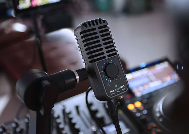 Microphones Black microphone attached to a stand, next to audio equipment with knobs and screens.