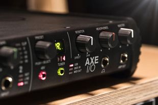 Interfaces Black Axe I/O audio interface with knobs, inputs, and output jacks, on a wooden surface.