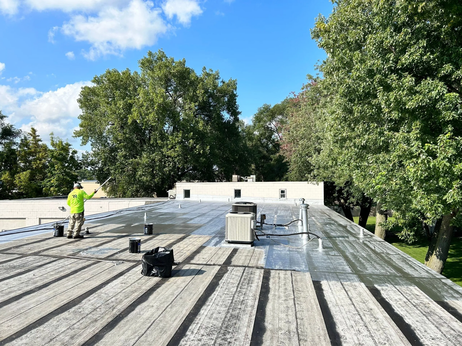 A man is standing on top of a roof painting it.