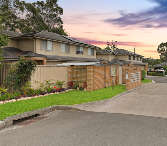 Row of townhouses with brick and tan facades, green lawn, and dusk sky.