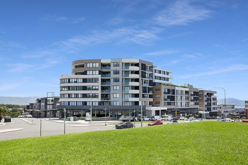 Modern multi-story apartment building on a sunny day with a green grassy area in the foreground.