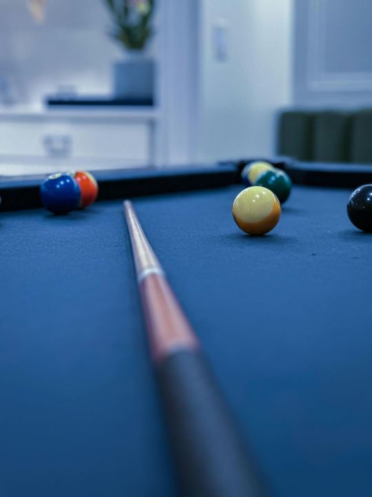 Pool balls scattered on a blue billiards table, viewed along a cue stick.