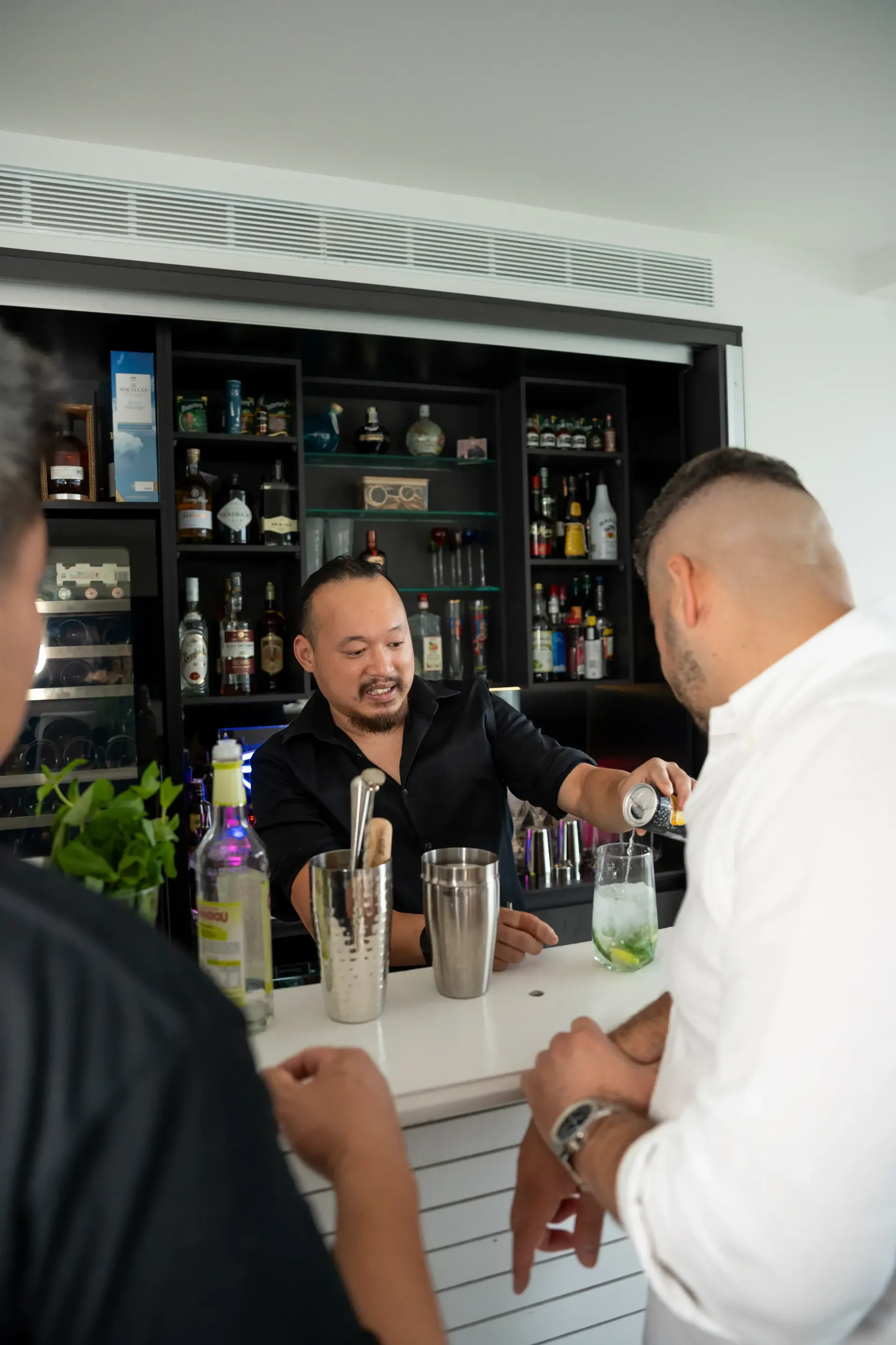 People chatting at a bar, with a bartender serving a drink behind the counter.