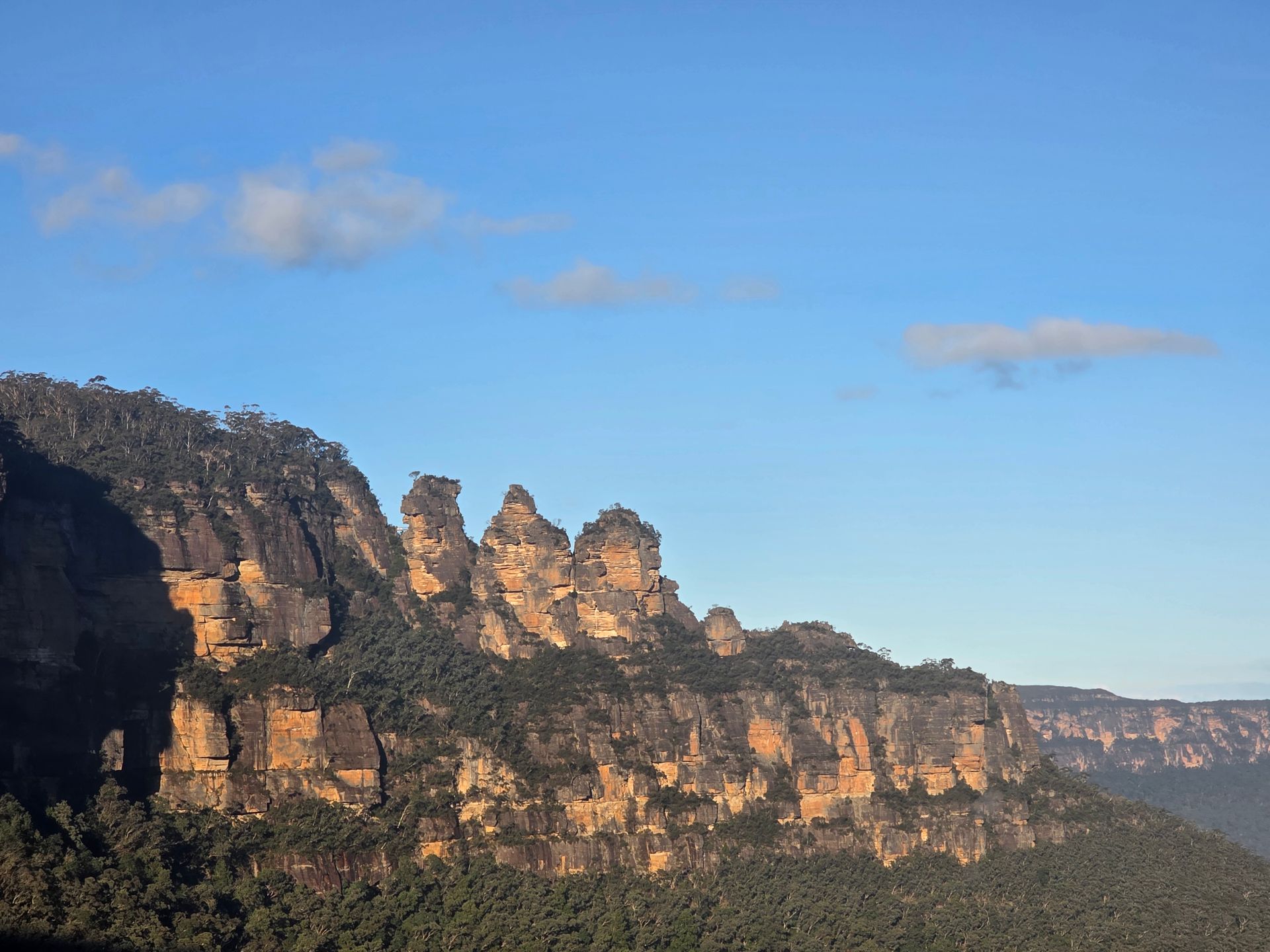 Sunlit sandstone cliffs under a blue sky with a few clouds