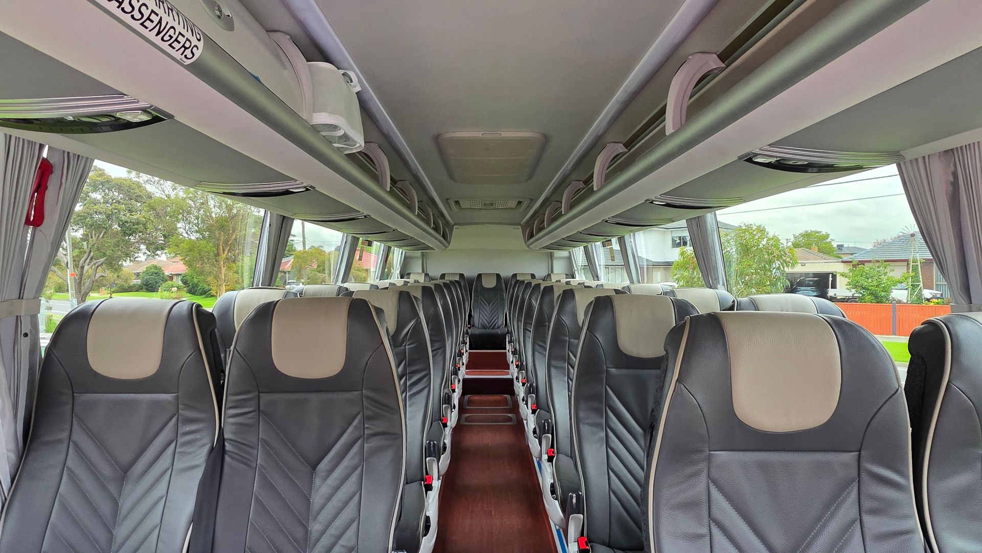 Empty coach bus interior with rows of gray seats and a central aisle, viewed from the front toward the back