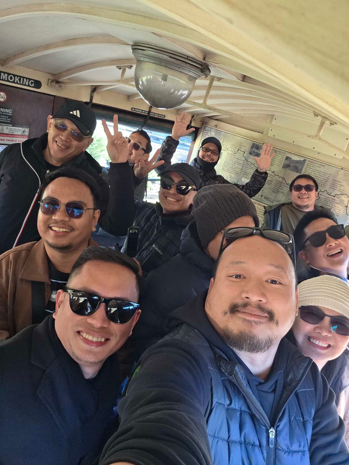 Group of smiling friends posing together inside a vehicle, wearing sunglasses and jackets.