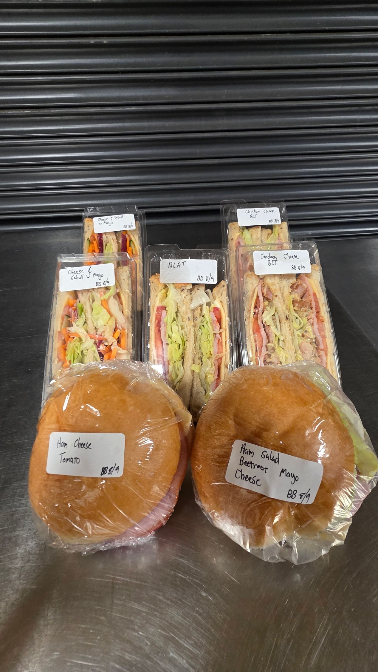 Two wrapped sandwiches and two wrapped buns on a metal counter against a black shutter.