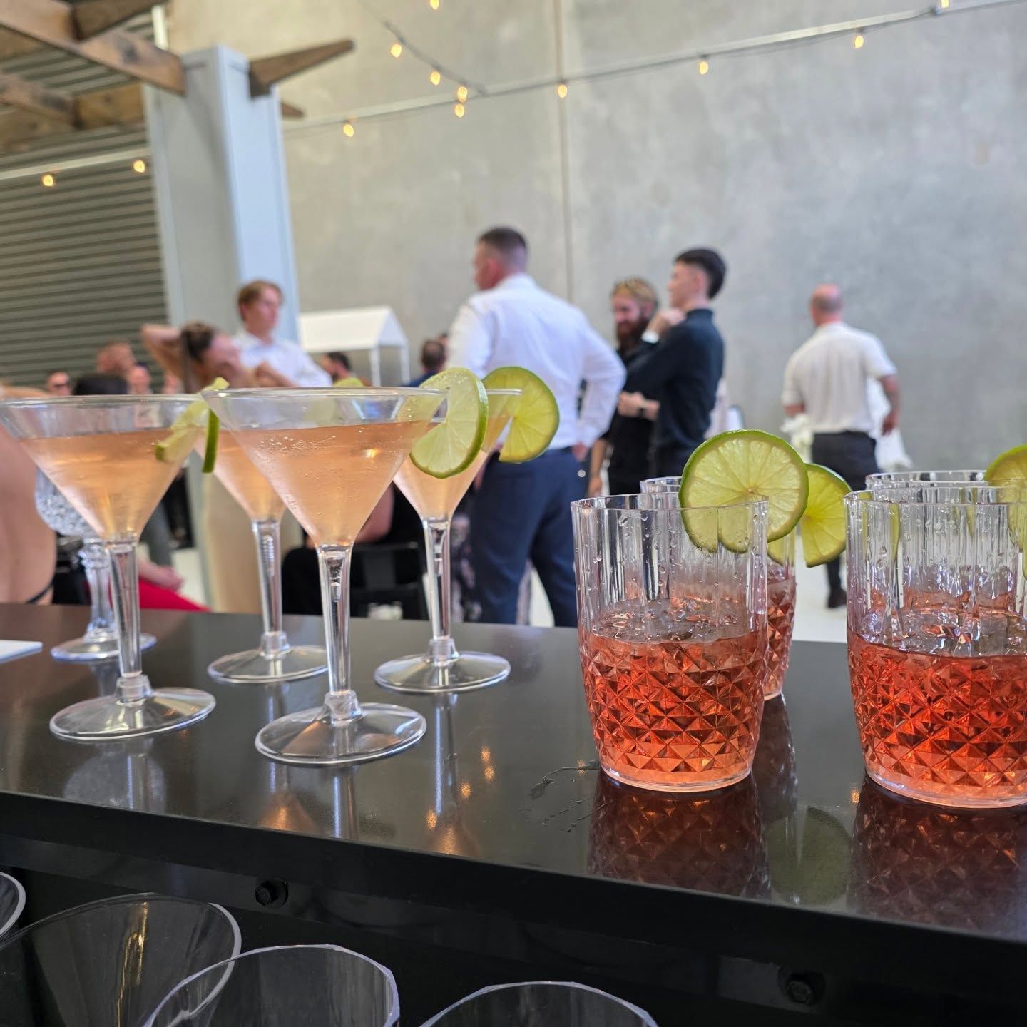 Cocktail glasses with lime on a bar counter at an indoor party with people mingling in the background