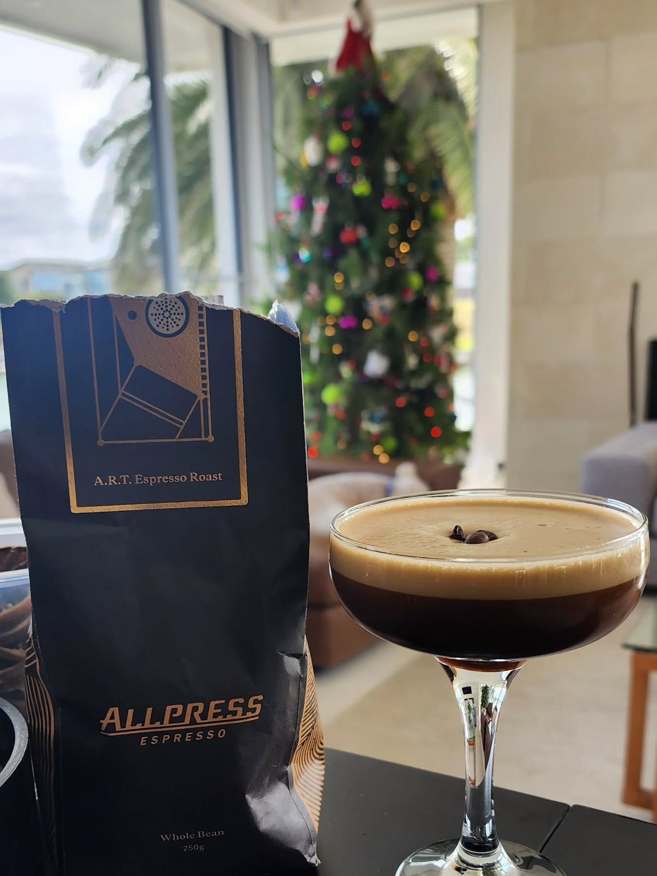 Espresso martini beside a dark coffee bag, with a decorated Christmas tree in the background