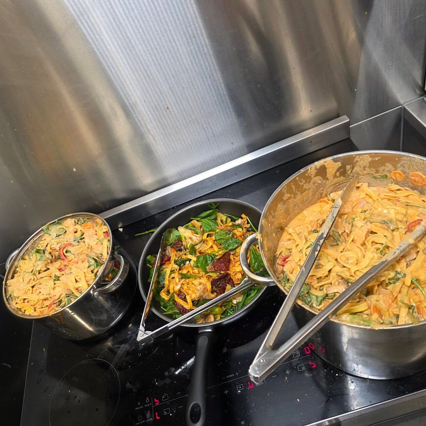 Three buffet trays of Indian curry and rice with serving spoons on a stainless steel counter.