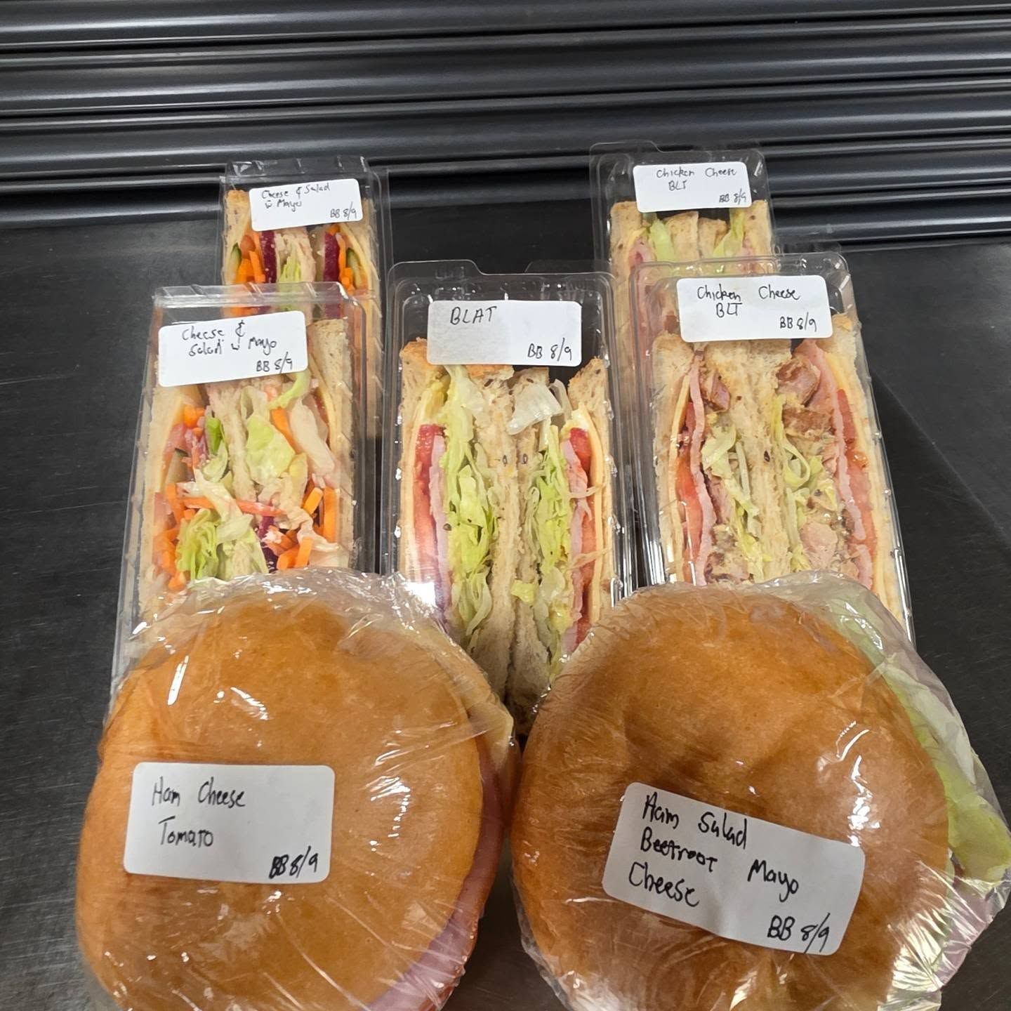 Packaged sandwiches and bread rolls displayed on a shelf with price labels.