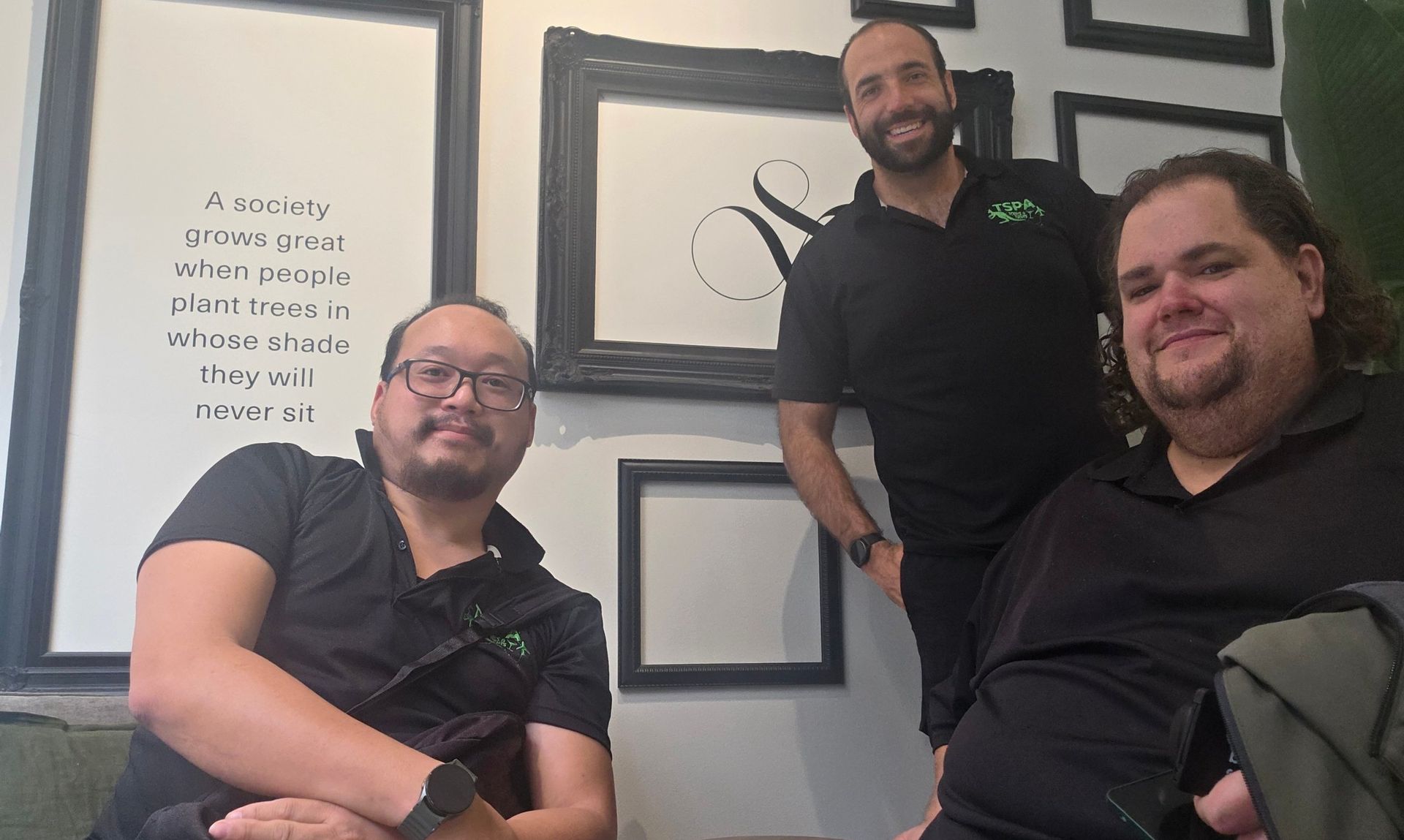 Three people smiling in an office, seated and standing in front of framed wall art.