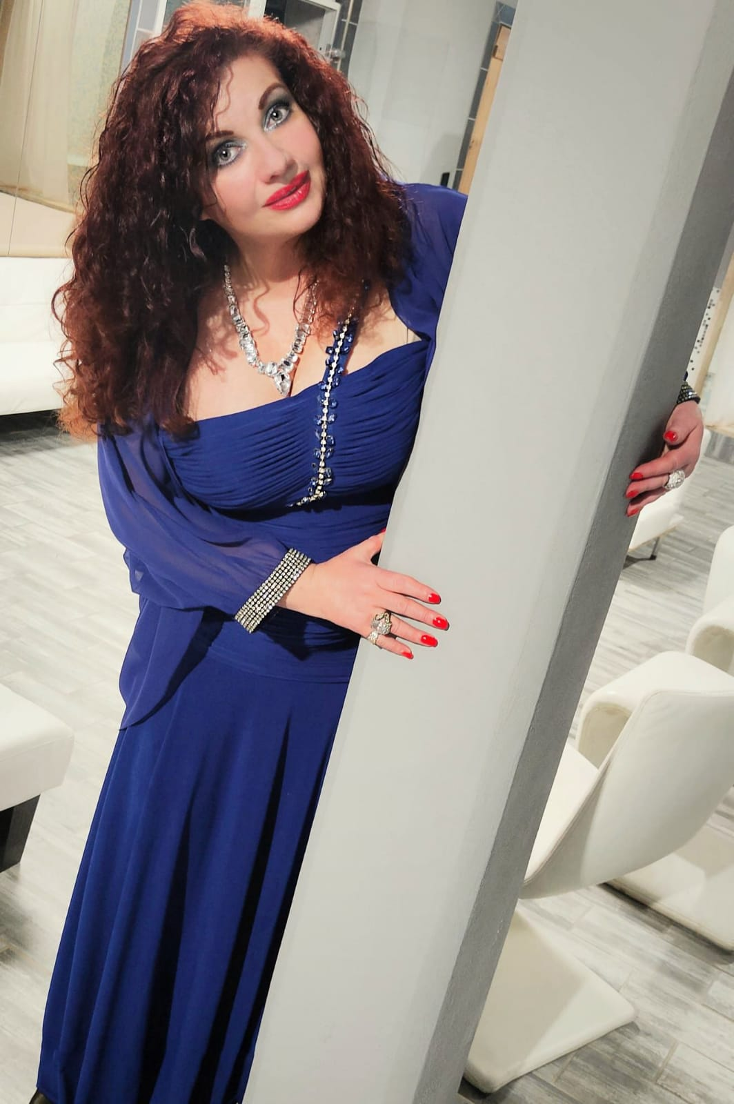 Donna in abito blu reale in posa accanto a una porta in una stanza luminosa
