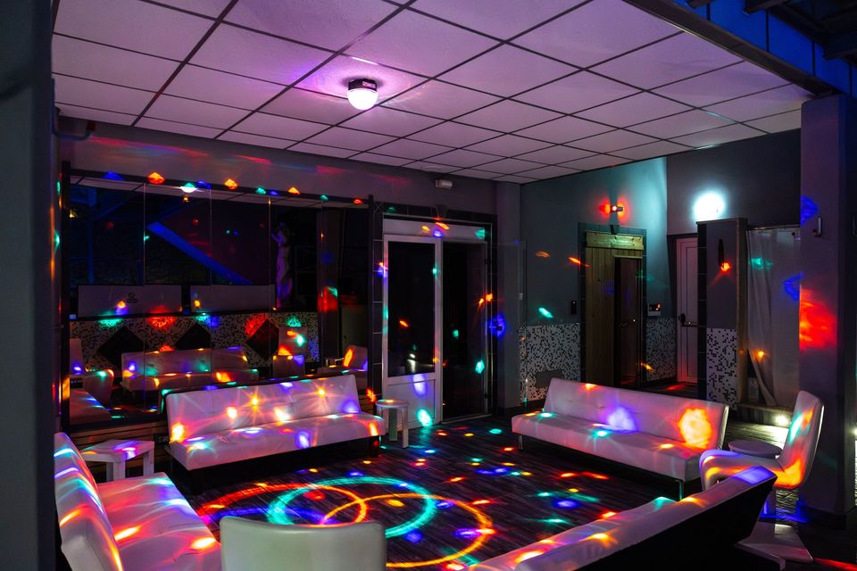 Luci da discoteca colorate sopra un moderno salotto con divani, un tavolo e grandi finestre di notte