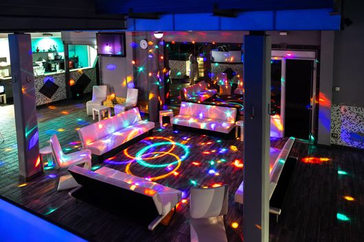 Luci da discoteca colorate illuminano un patio con posti a sedere e motivi luminosi sul pavimento.