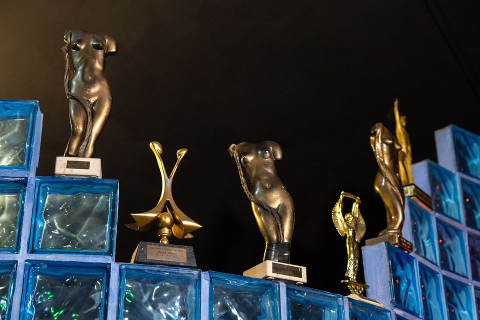 Statuette di riconoscimento in oro e argento esposte su blocchi di vetro blu su uno sfondo scuro.
