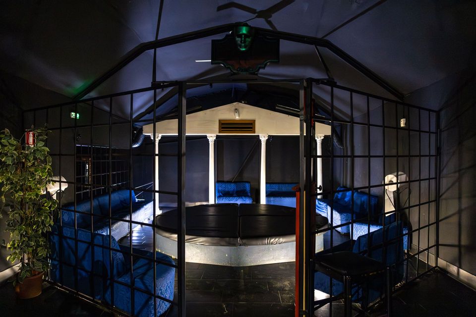 Piscina circolare interna, scarsamente illuminata e con acqua blu, visibile attraverso un cancello di metallo nero in una stanza simile a una serra.
