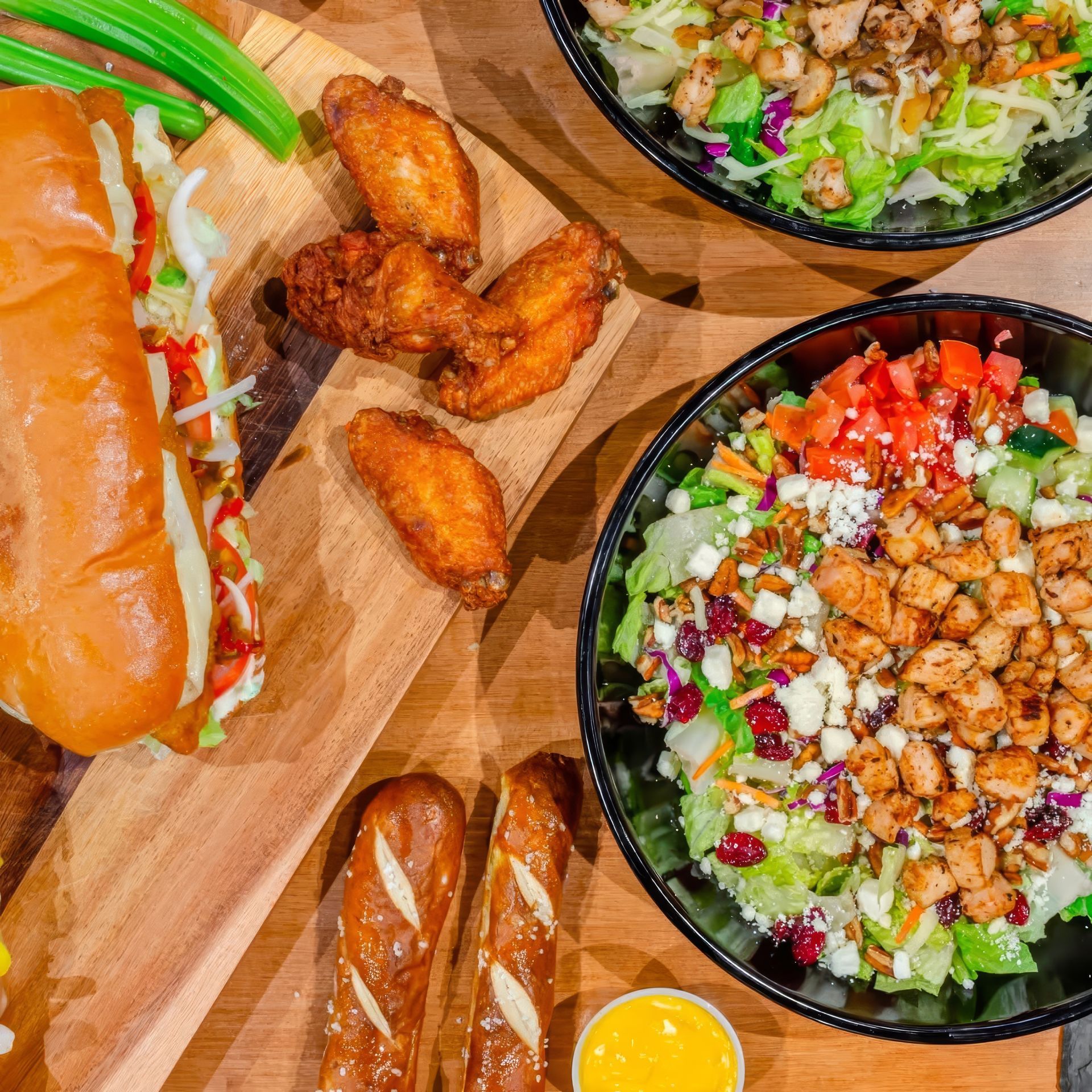 Assorted sushi, fried chicken wings, and two salad bowls arranged on a wooden board
