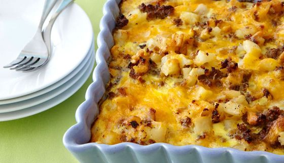 Baked casserole in a white scalloped dish beside stacked white plates and a fork on a green tablecloth