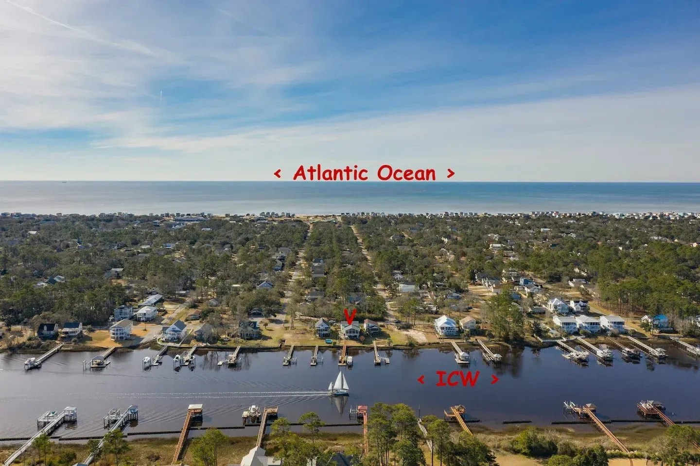 Aerial view of a coastal marina and neighborhood with boats on a lagoon beside the Atlantic Ocean.