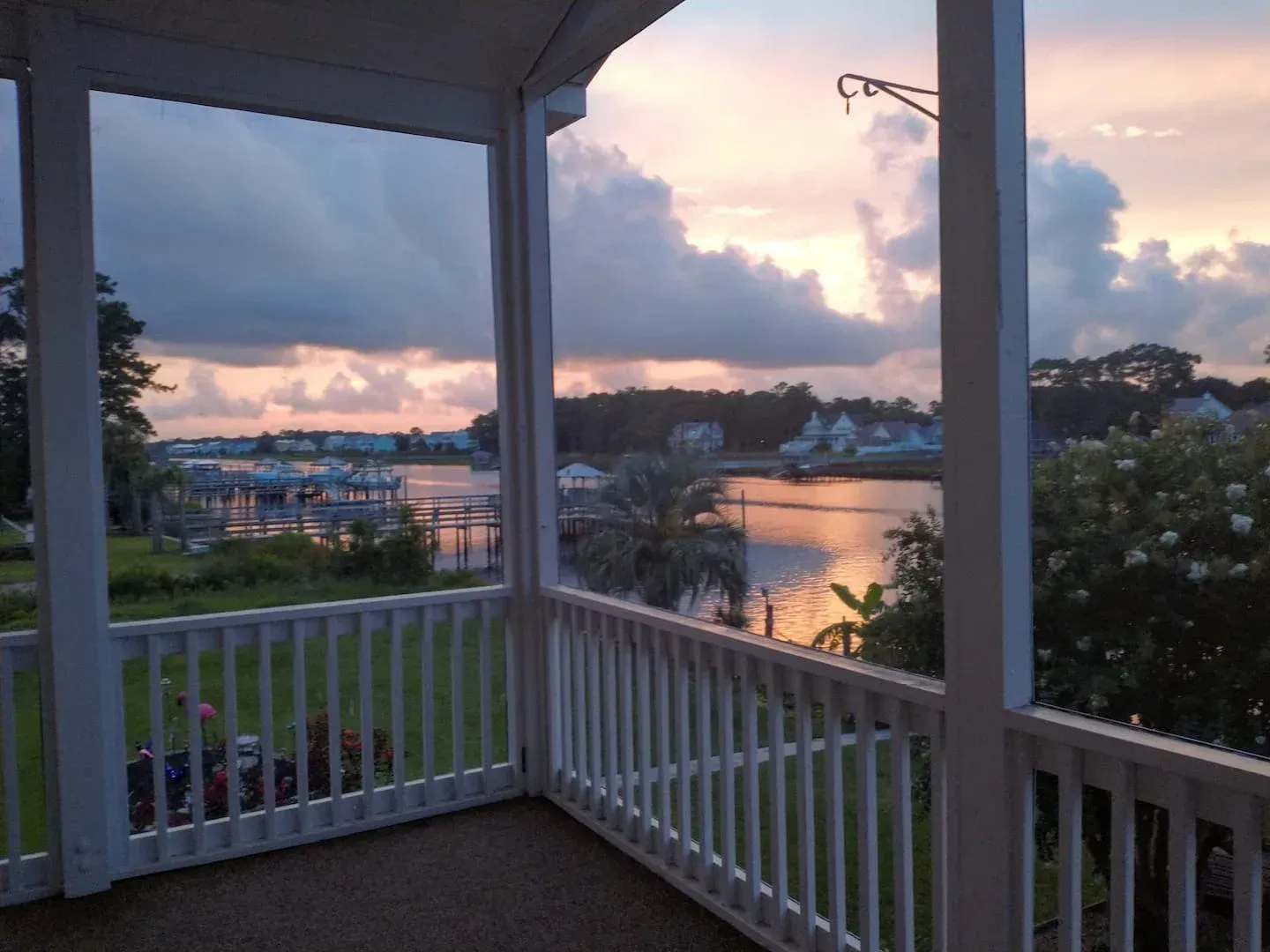 Porch overlooking a calm waterfront at sunset with pink clouds and palm trees