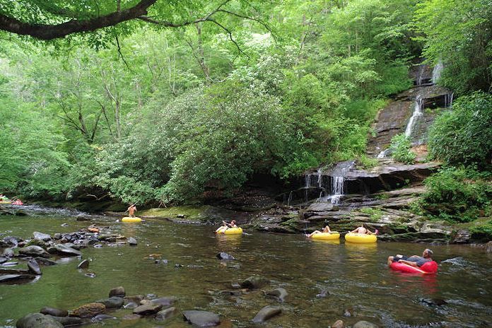 Kayakers on a calm forest stream beside a small waterfall and lush green trees