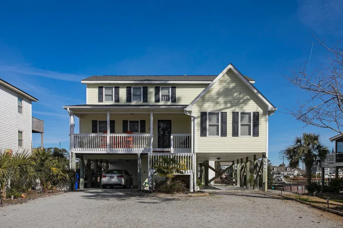Two-story cream house with porch, raised on stilts, under a clear blue sky