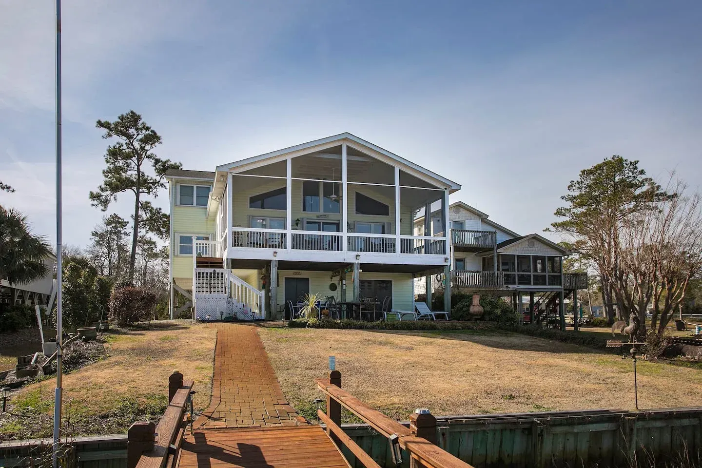 White waterfront house with blue trim, dock, and wooden walkway under a clear sky