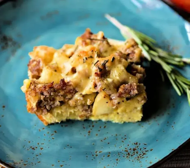 Slice of cheesy casserole on a blue plate with rosemary garnish