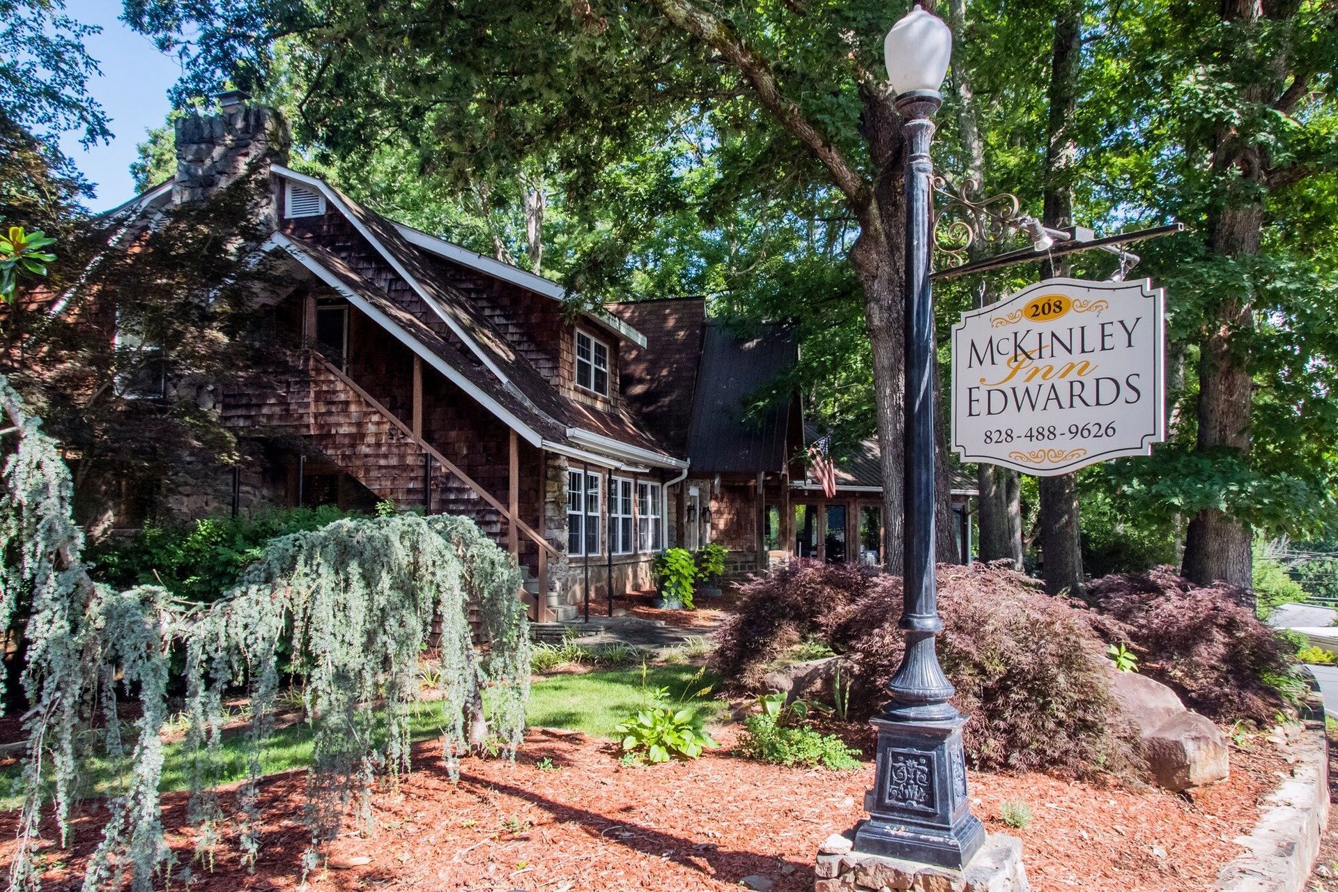 Rustic winery entrance with sign, lamp post, and lush greenery amid red mulch