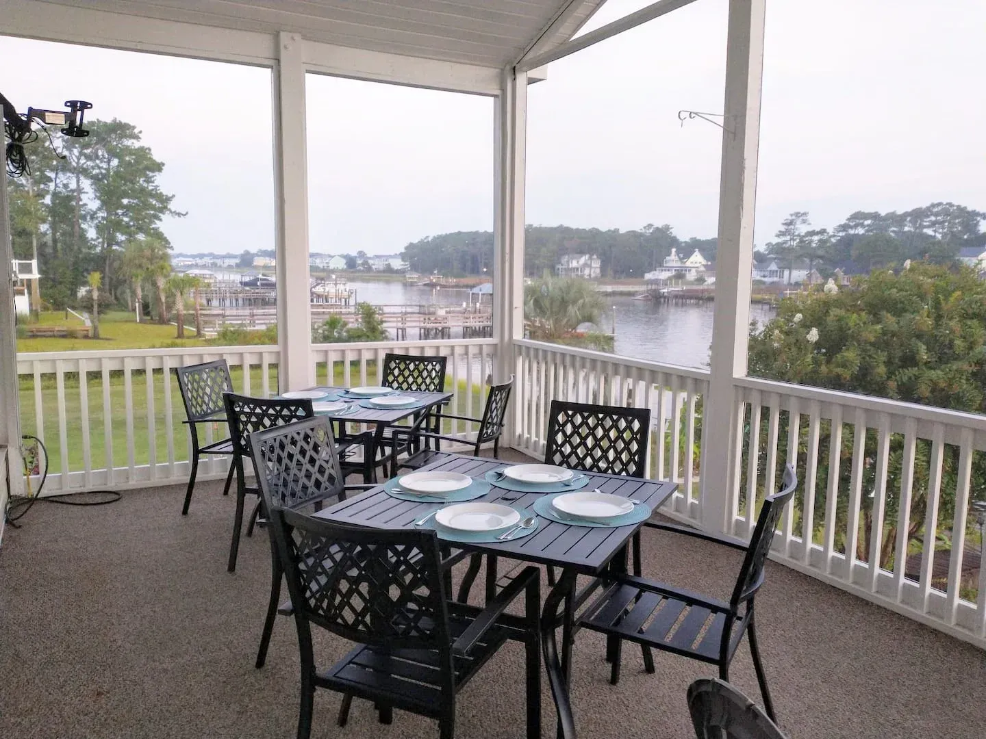 Covered porch with black patio dining set overlooking a calm waterfront.