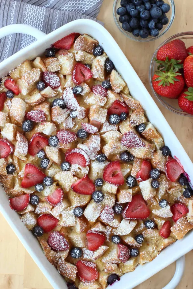 Strawberry-topped baked dessert in a white dish, with blueberries and strawberries beside it.