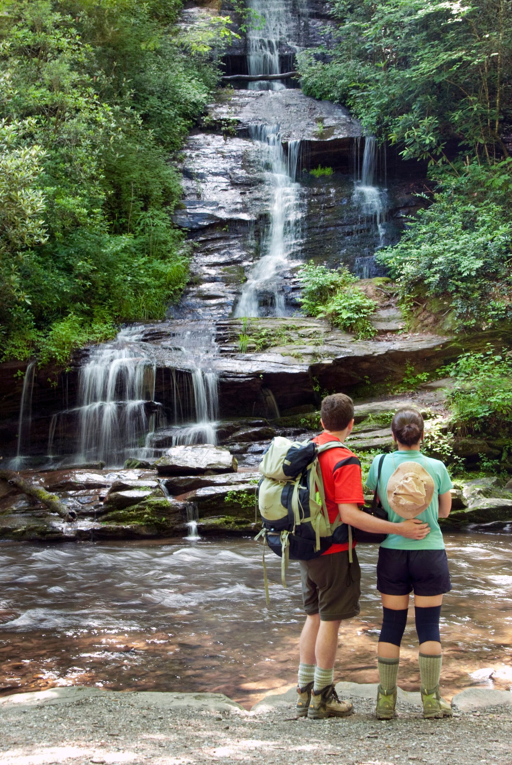 Two hikers with backpacks standing by a forest waterfall