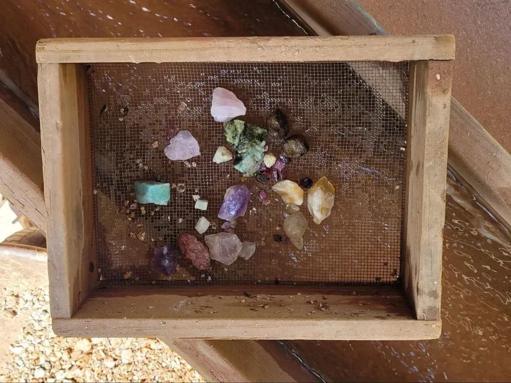 Small wooden box with a mesh back holding assorted colorful crystals and stones.