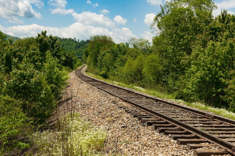 Curving railroad tracks through green trees under a blue sky with clouds