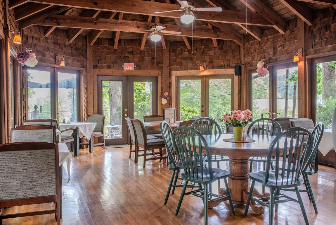 Rustic dining room with wooden tables and chairs, large windows, and warm natural light