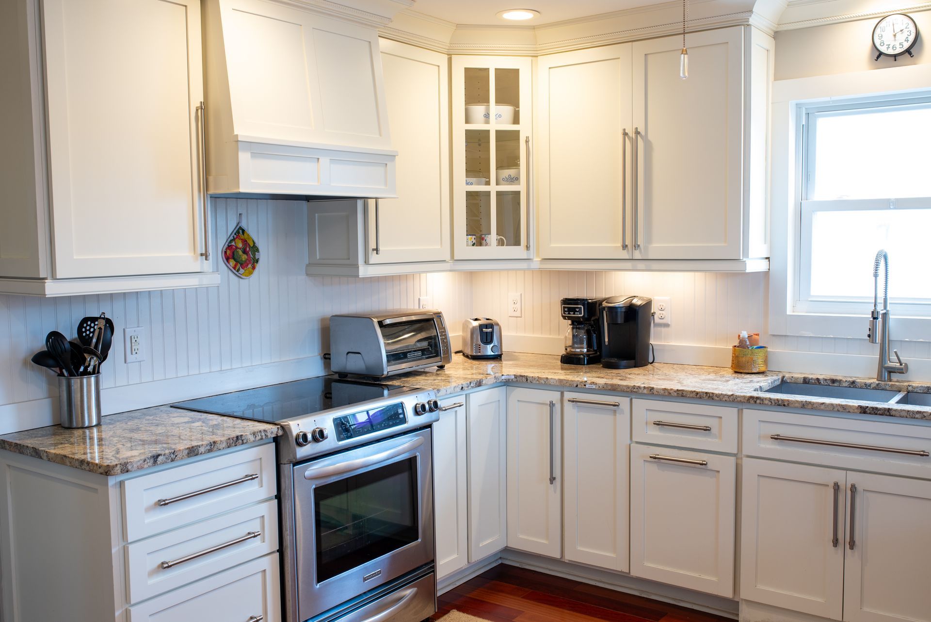 Bright white kitchen with granite counters, stainless stove, cabinets, and a window over the sink