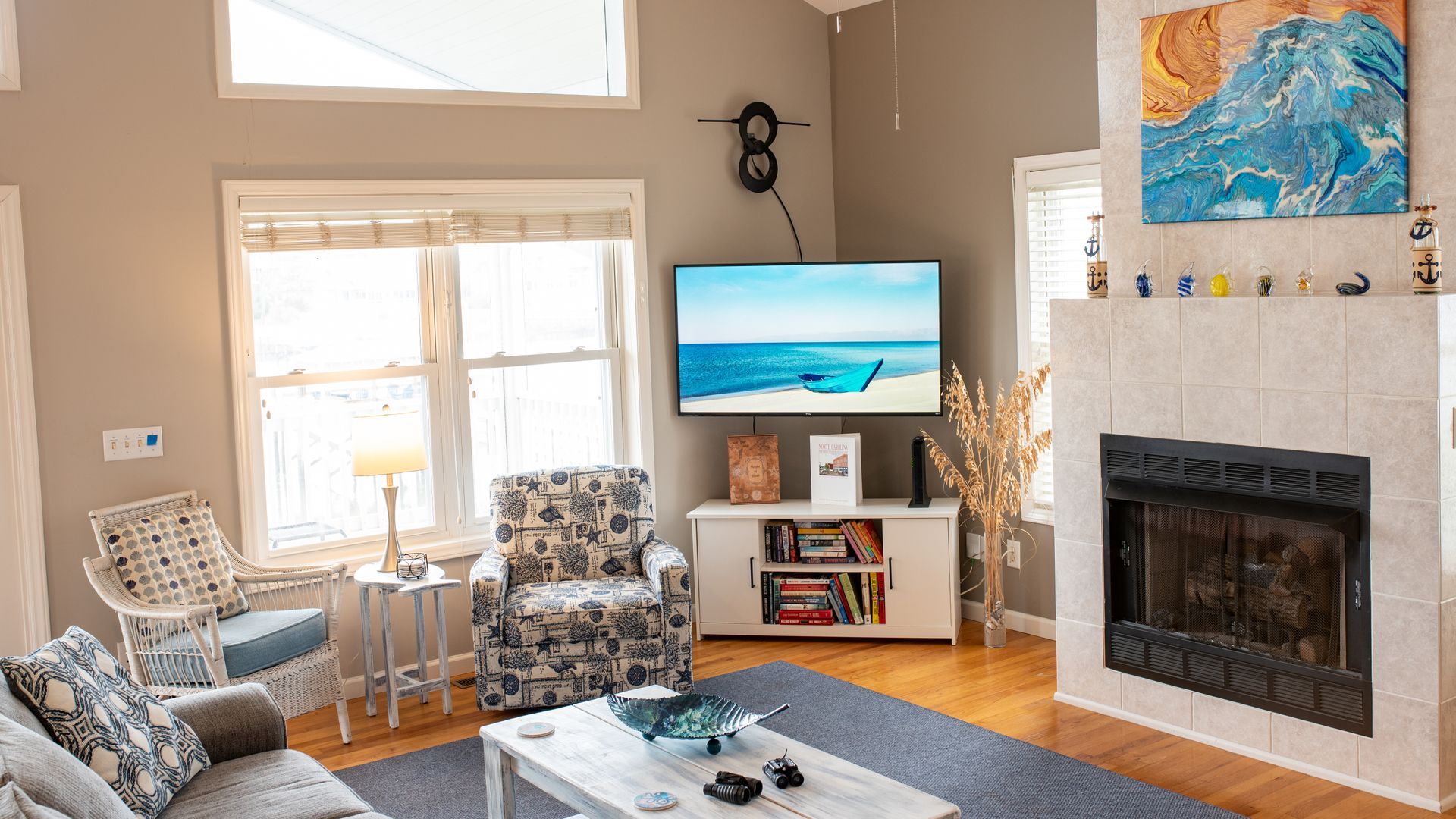 Bright living room with fireplace, TV, large windows, patterned chairs, and blue rug.