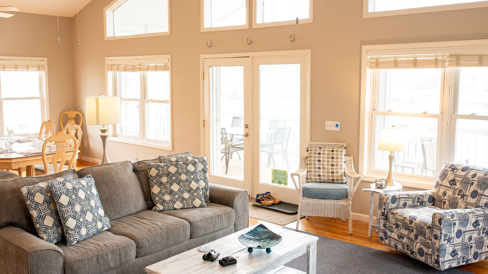 Bright living room with gray sofa, floral armchair, white coffee table, and large windows with sheer curtains