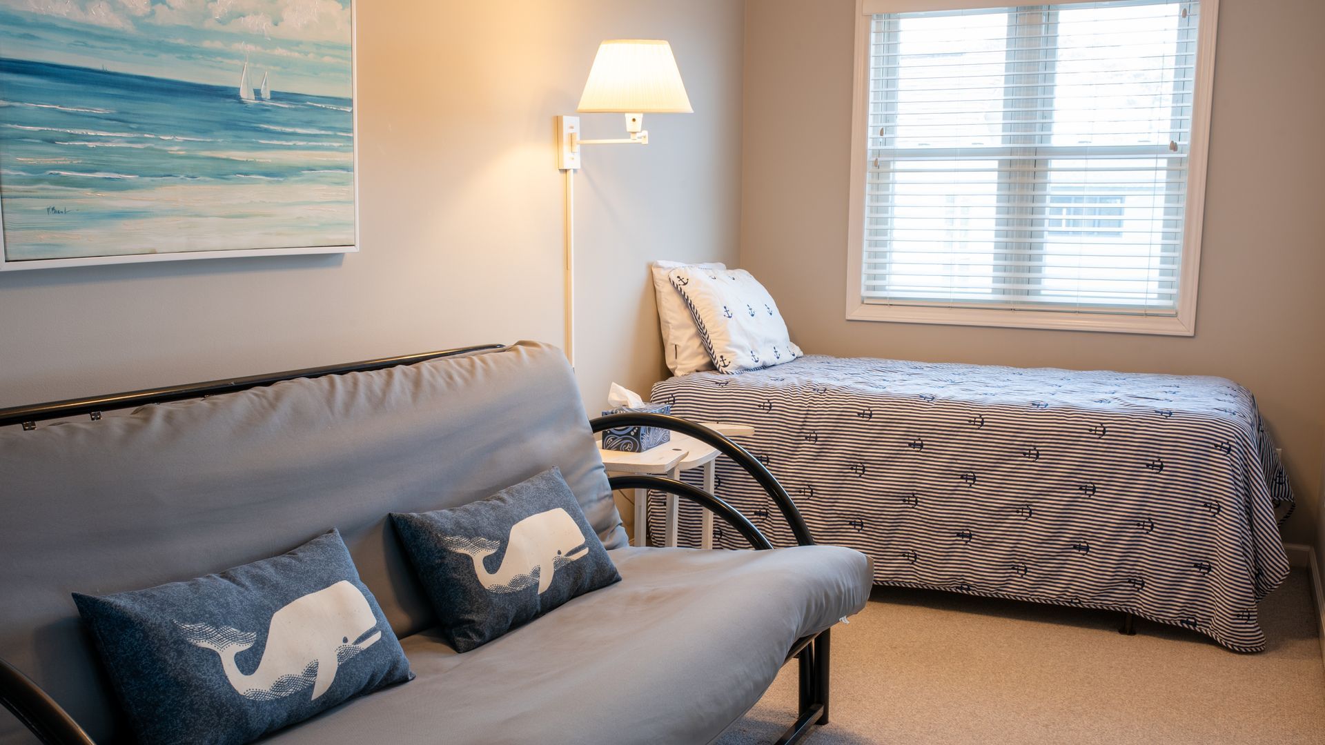 Cozy bedroom with a striped bed, gray futon, floor lamp, and window with blinds